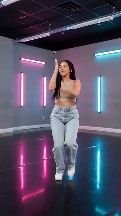 Quadro de vídeo externo de uma pessoa dançando sozinha de jeans e tênis brancos, levantando um braço e um pé em um estúdio neon rosa e ciano